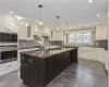 Kitchen featuring built in microwave, oven, decorative light fixtures, a kitchen island with sink, and white cabinets