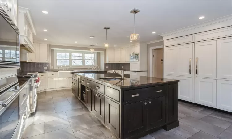 Kitchen featuring sink, tasteful backsplash, decorative light fixtures, a kitchen island with sink, and appliances with stainless steel finishes