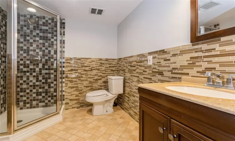 Bathroom with walk in shower, vanity, tile walls, tile patterned flooring, and toilet