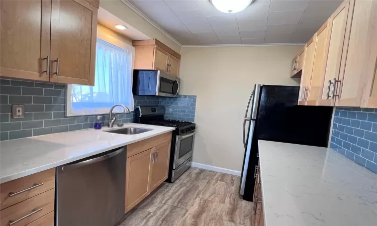 Kitchen featuring light stone countertops, sink, stainless steel appliances, tasteful backsplash, and crown molding