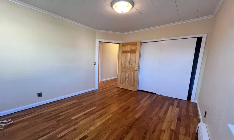 Bedroom 2 with baseboard heating, dark hardwood / wood-style flooring, crown molding, and a closet