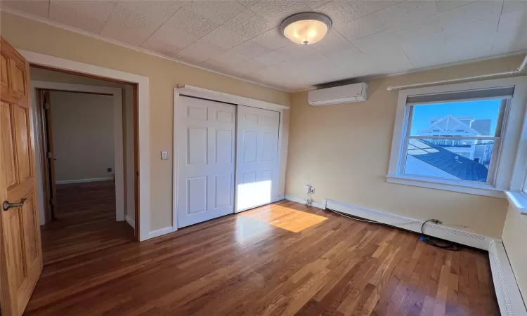 Bedroom 1 featuring an AC wall unit, crown molding, a closet, and dark wood-type flooring