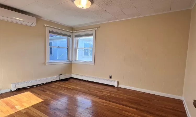 Bedroom 1 with dark hardwood / wood-style floors, ornamental molding, baseboard heating, and a wall unit AC