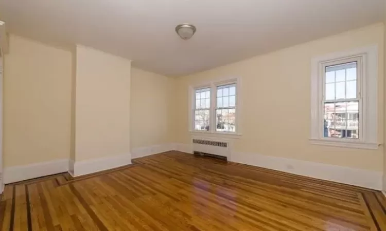 Empty room with dark hardwood / wood-style flooring and radiator