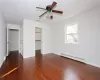 Unfurnished bedroom featuring ceiling fan, a walk in closet, baseboard heating, and dark wood-type flooring