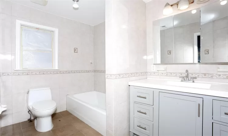 Bathroom featuring tile patterned flooring, vanity, toilet, and tile walls