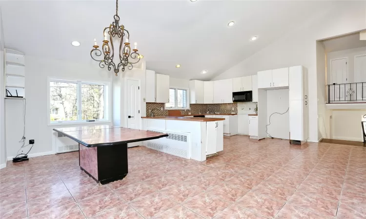 Kitchen with hanging light fixtures, a kitchen island, high vaulted ceiling, a chandelier, and white cabinets