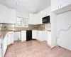 Kitchen featuring black appliances, light tile patterned flooring, white cabinetry, and sink