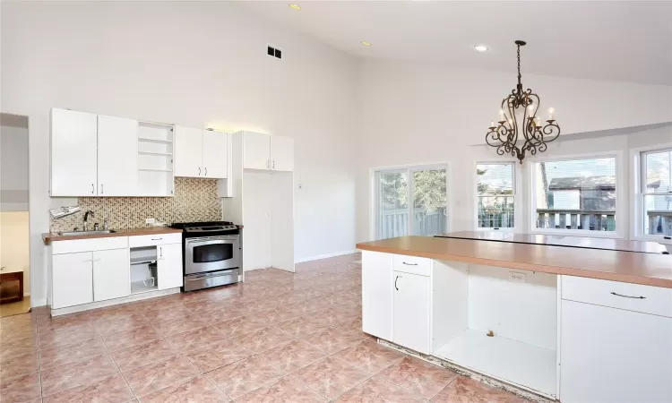 Kitchen featuring white cabinetry, stainless steel range, high vaulted ceiling, and decorative light fixtures