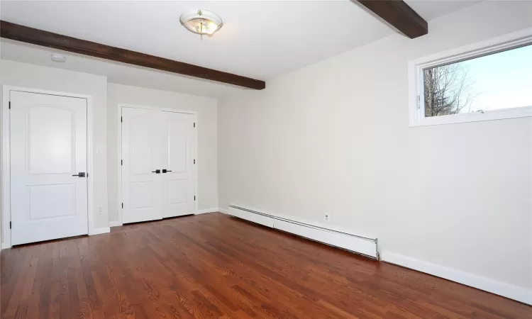 Unfurnished bedroom with dark wood-type flooring, beamed ceiling, and a baseboard radiator