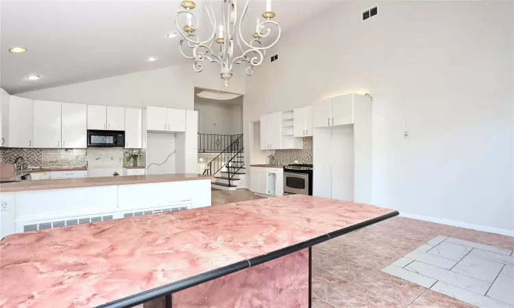 Kitchen with high vaulted ceiling, stainless steel stove, decorative backsplash, decorative light fixtures, and white cabinetry