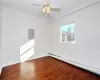 Unfurnished room with hardwood / wood-style flooring, ceiling fan, electric panel, and a baseboard heating unit