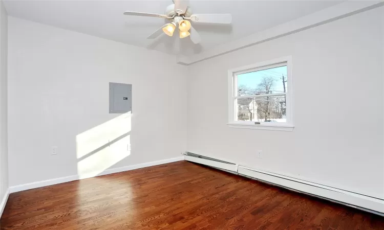 Unfurnished room with hardwood / wood-style flooring, ceiling fan, electric panel, and a baseboard heating unit