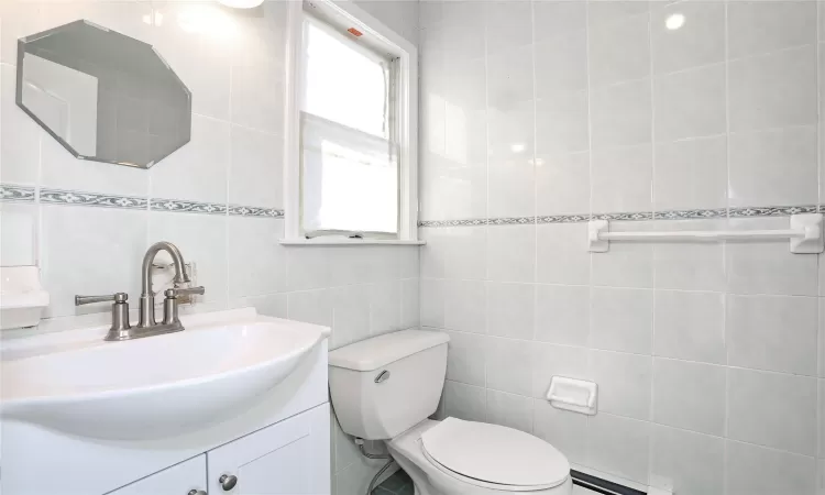 Bathroom featuring toilet, vanity, tile walls, and a baseboard heating unit