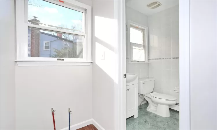 Bathroom with a baseboard heating unit, toilet, tile walls, and a healthy amount of sunlight