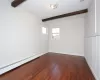 Unfurnished room with beamed ceiling, dark wood-type flooring, and a baseboard heating unit