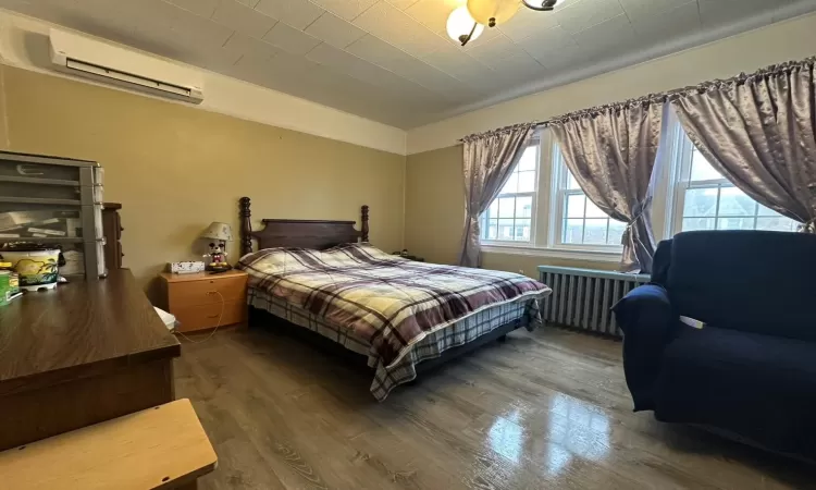 Bedroom featuring a wall mounted air conditioner, wood-type flooring, and radiator