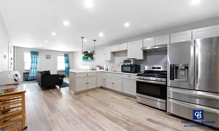 Kitchen with white cabinetry, hanging light fixtures, stainless steel appliances, and light wood-type flooring