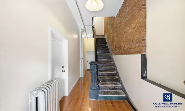 Stairs with hardwood / wood-style floors, radiator, and brick wall