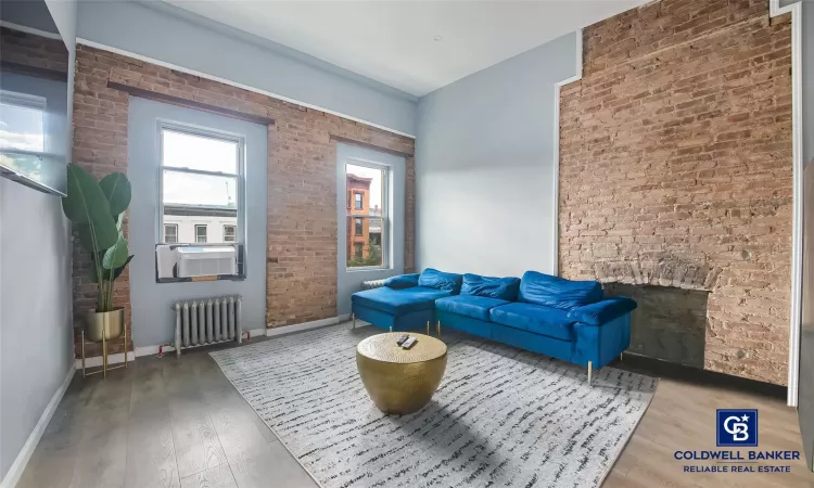 Sitting room featuring brick wall, wood-type flooring, radiator, and cooling unit