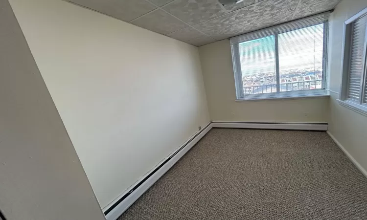 Unfurnished room with a paneled ceiling, carpet, and a baseboard heating unit