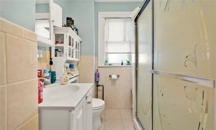 Bathroom with walk in shower, vanity, tile walls, tile patterned flooring, and toilet