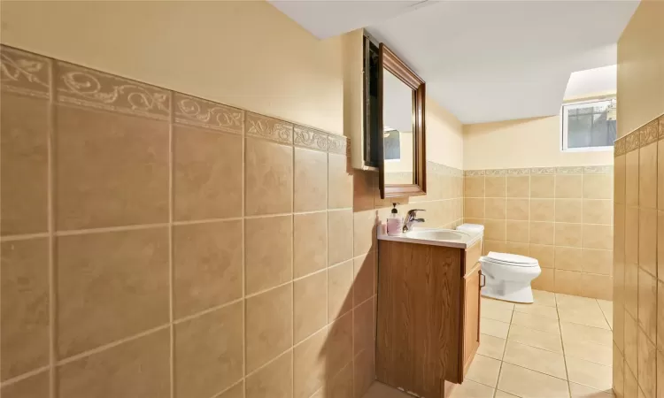 Bathroom featuring tile patterned flooring, vanity, toilet, and tile walls