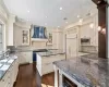 Kitchen with custom exhaust hood, sink, built in appliances, decorative light fixtures, and dark stone countertops