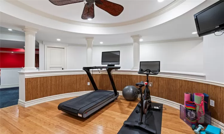 Workout room featuring hardwood / wood-style floors, ceiling fan, wood walls, and crown molding