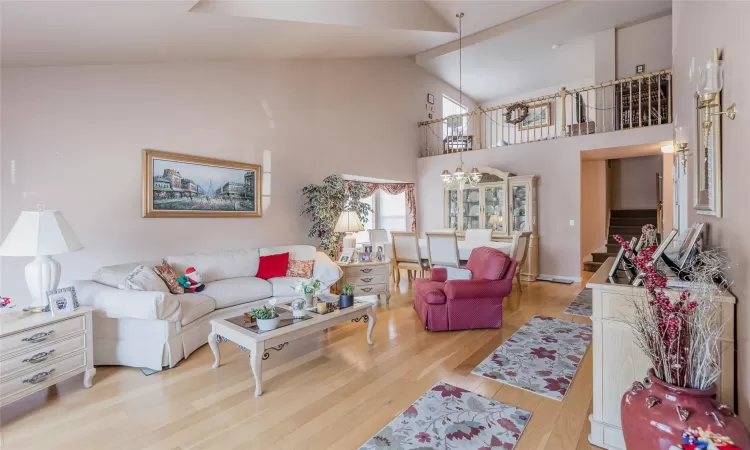 Living room with light wood-type flooring, high vaulted ceiling, and a chandelier