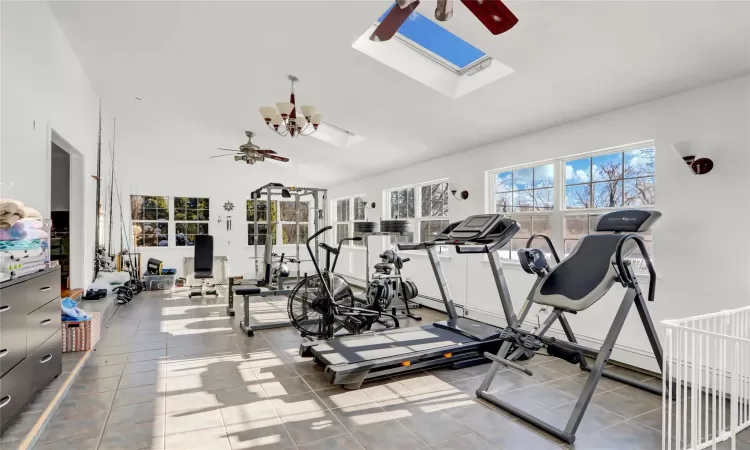 Gym with ceiling fan, lofted ceiling with skylight, and tile patterned flooring