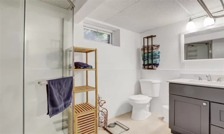 Bathroom with tile patterned flooring, vanity, an enclosed shower, a drop ceiling, and toilet