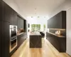 Kitchen featuring a kitchen bar, decorative backsplash, double oven, a spacious island, and light hardwood / wood-style flooring