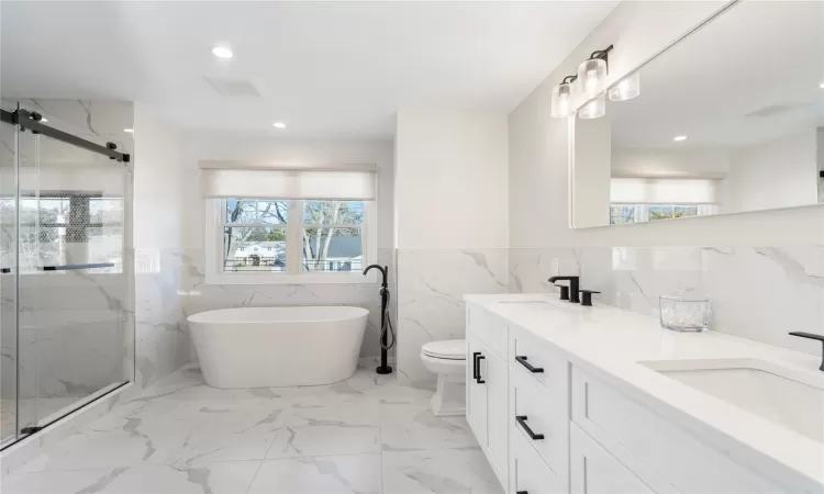 Full bathroom with tile walls, shower with separate bathtub, vanity, and toilet