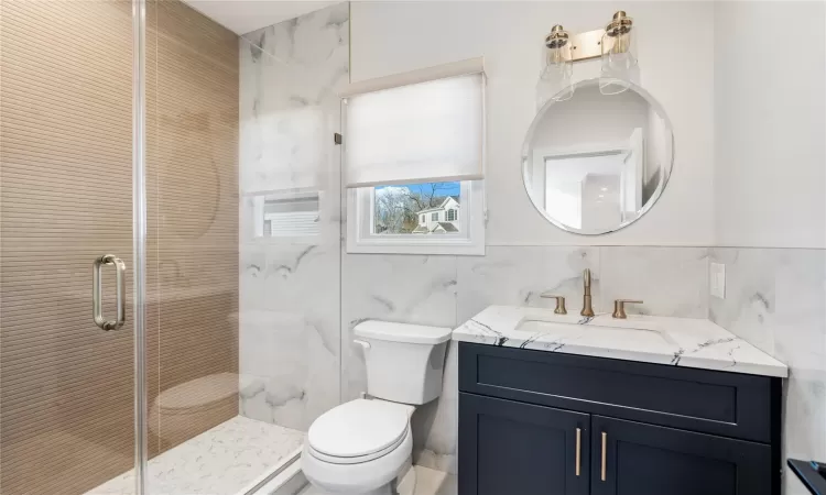 Bathroom featuring tile walls, vanity, a shower with shower door, and toilet