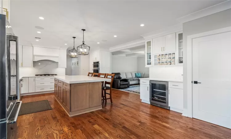 Kitchen with a kitchen island, wine cooler, white cabinetry, appliances with stainless steel finishes, and ornamental molding