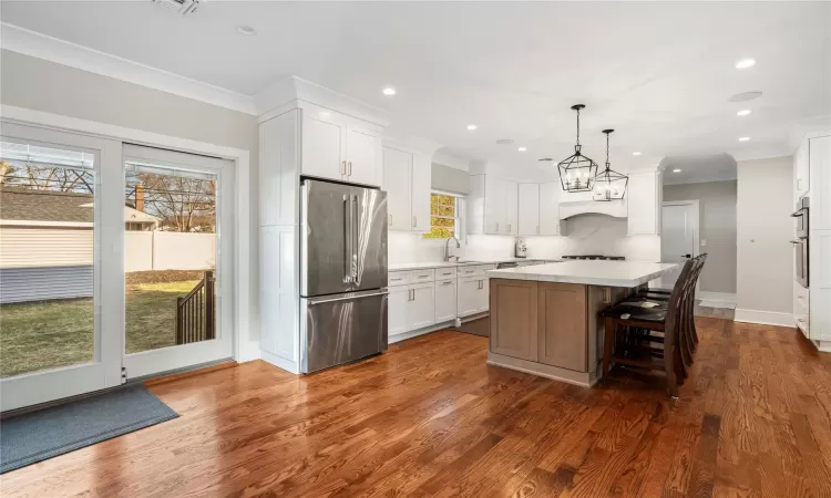 Kitchen featuring dark wood-type flooring, a center island, decorative light fixtures, white cabinets, and appliances with stainless steel finishes