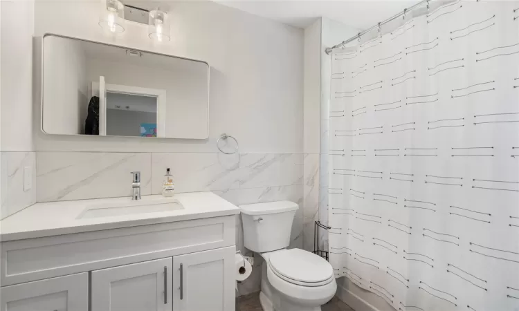 Bathroom featuring tile walls, toilet, and vanity