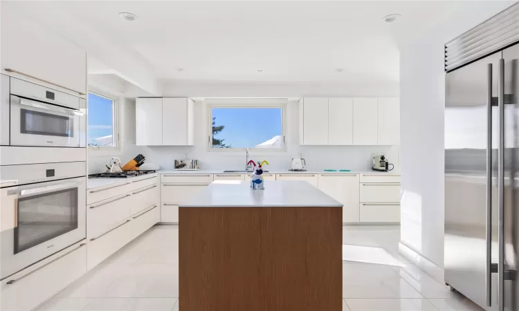 Kitchen featuring sink, light tile patterned floors, a kitchen island, white cabinetry, and stainless steel appliances