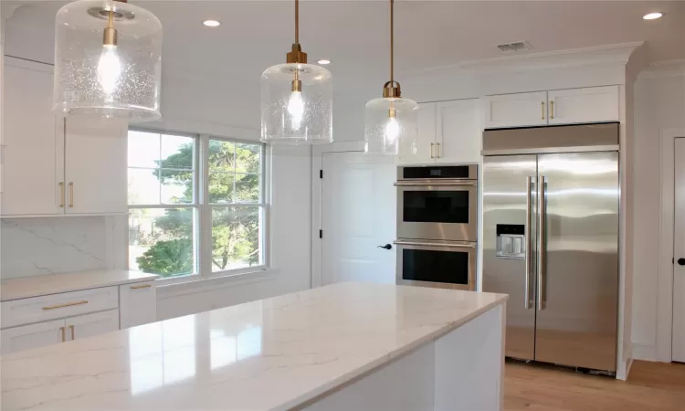 Kitchen with pendant lighting, decorative backsplash, light stone counters, and stainless steel appliances