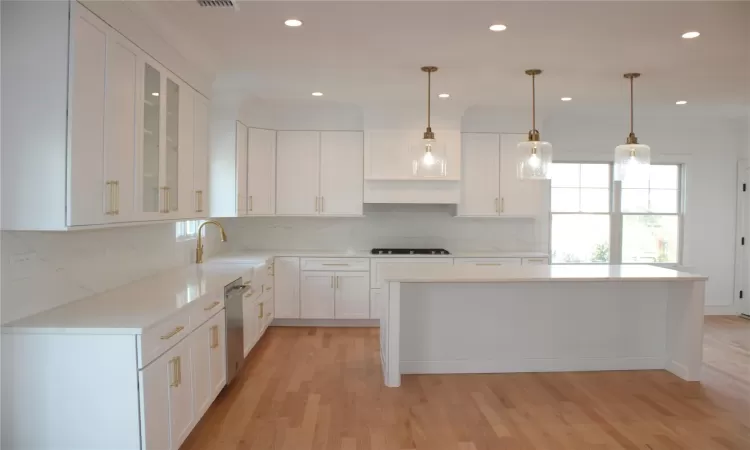 Kitchen featuring light wood-type flooring, tasteful backsplash, sink, decorative light fixtures, and white cabinets