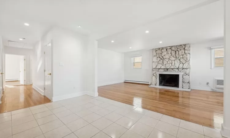 Unfurnished living room featuring an AC wall unit, a fireplace, light tile patterned flooring, and a baseboard radiator