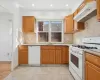 Kitchen featuring backsplash, white appliances, sink, light tile patterned floors, and range hood