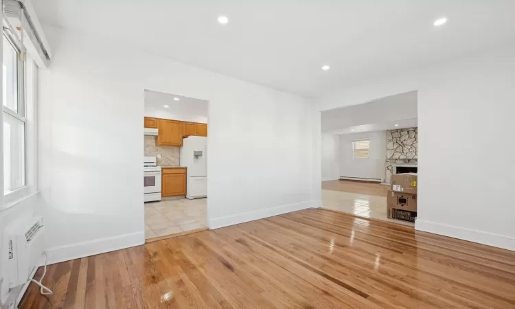 Unfurnished living room featuring a wall mounted air conditioner, light hardwood / wood-style floors, a stone fireplace, and a baseboard heating unit