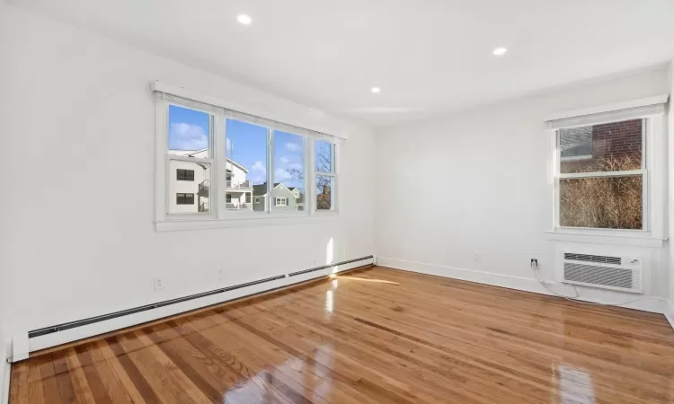 Empty room featuring a wall mounted air conditioner, baseboard heating, and hardwood / wood-style flooring