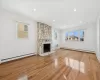 Unfurnished living room with an AC wall unit, a stone fireplace, light wood-type flooring, and a baseboard heating unit