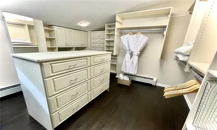 Primary bedroom closet featuring dark wood-type flooring and a baseboard heating unit