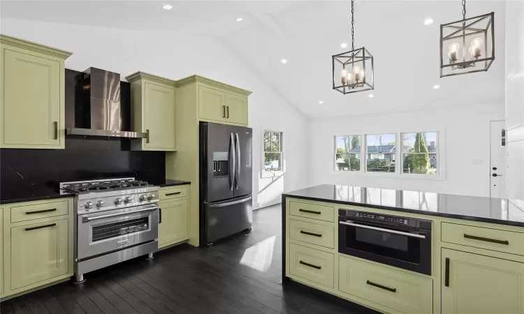 Kitchen featuring wall chimney exhaust hood, decorative light fixtures, tasteful backsplash, lofted ceiling, and appliances with stainless steel finishes