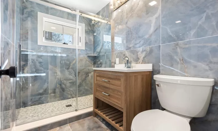 Bathroom with tile walls, an enclosed shower, toilet, and vanity