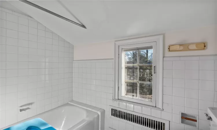 Bathroom featuring lofted ceiling, radiator heating unit, tile walls, and a washtub